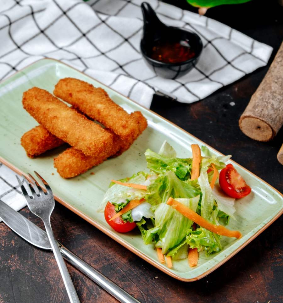 Palitos crujientes de pescado servidos con ensalada fresca de lechuga y tomates cherry en un plato