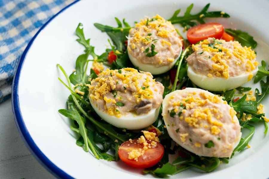 Huevos rellenos de atún servidos sobre una cama de rúcula con tomates cherry