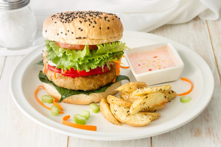 Hamburguesa de pescado servida con papas al horno y salsa para mojar en un plato