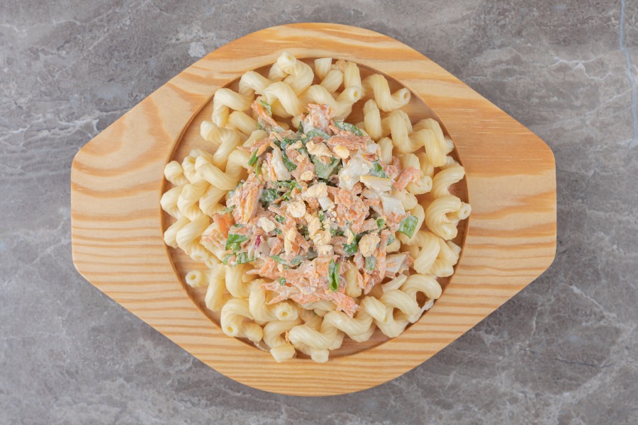 Macarrones con salsa de atún, servidos en un plato de madera sobre una mesa de mármol