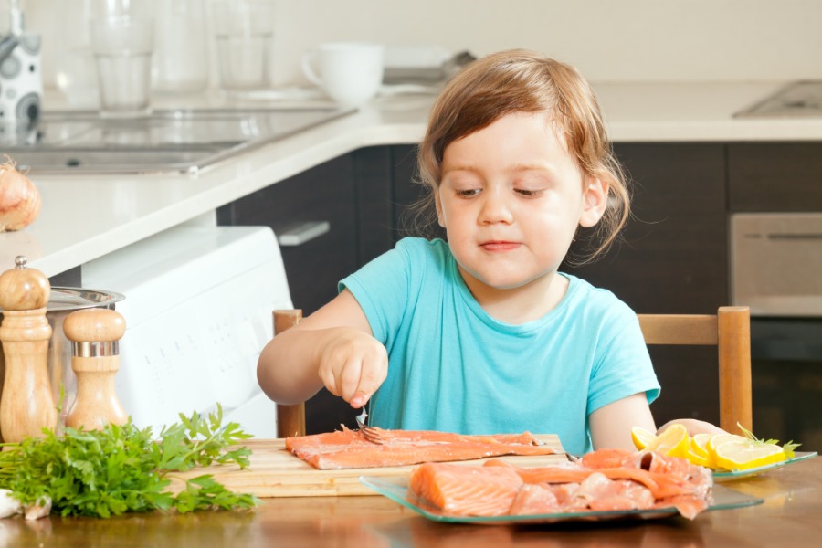 Niña pequeña preparando pescado en la cocina con cuidado, mientras ayuda a cocinar