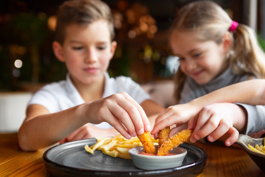 Niños disfrutando de palitos de pescado empanizados acompañados de papas fritas y salsa para mojar